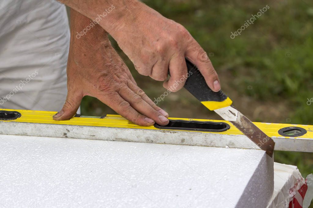 Close-up of worker hand with knife and level cutting white rigid polyurethane foam sheet for house insulation. Modern technology, renovation, professional job, alternative for mineral wool concept.