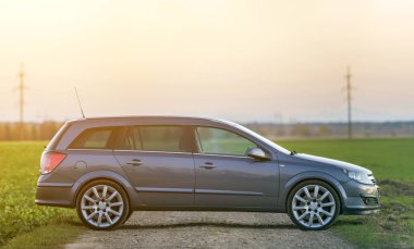 Gri gümüş boş araba çakıl kırsal yol boyunca üzerinde park etmiş yeşil çayırlar, uzak şehir bina ve açık gökyüzü kopya alan arka plan bulanık. Ulaşım, seyahat, Araçlar tasarım konsepti.