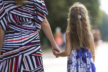 Oldukça küçük sarı uzun saçlı çocuk kız moda renkli elbise holding arka görmek trustingly el bulanık renkli güneşli yaz bokeh arka plan üzerine açık havada Genç kadın.