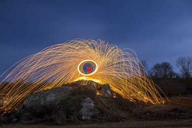 Uzun pozlama bir havai fişek duş parlak sarı parlak parıldıyor, mavi gece gökyüzü arka plan üzerinde yapım bir dairede çelik yün iplik, kayalık tepe üzerinde duran adam vurdu. Işık resim sanat kavramı.