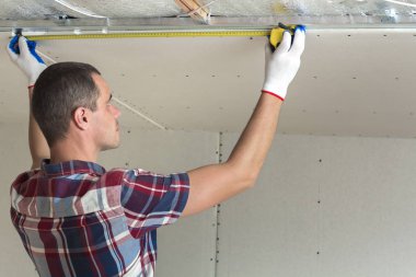 Yakışıklı delikanlı casual giyim Alçıpan Asma Tavan tavan yalıtımlı alüminyum folyo ile üzerinde metal çerçeve bağlı ölçümü alır. İnşaat, tadilat, DIT kavramı.