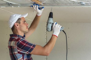 Her zamanki giyim ve iş eldivenleri Alçıpan sabitleme genç adam metal çerçeve parlak alüminyum folyo ile yalıtımlı tavanda Elektrikli tornavida kullanarak tavana askıya. DIY, kendiniz yapın kavramı.
