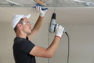 Alçıpan sabitleme Gözlük Genç adam metal çerçeve parlak alüminyum folyo ile yalıtımlı tavanda Elektrikli tornavida kullanarak tavana askıya. Tadilat, inşaat, do It yourself konsepti.