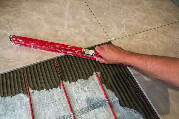 Ceramic tiles and tools for tiler. Worker hand installing floor tiles. Home improvement, renovation - ceramic tile floor adhesive, mortar, level.