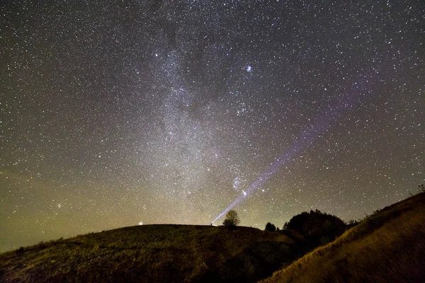 在美丽的深蓝色夏季星空下 在深绿色的青草山上 用手电筒的男人的小剪影 夜间摄影 美丽的自然概念 宽全景 复制空间背景 — 图库照片