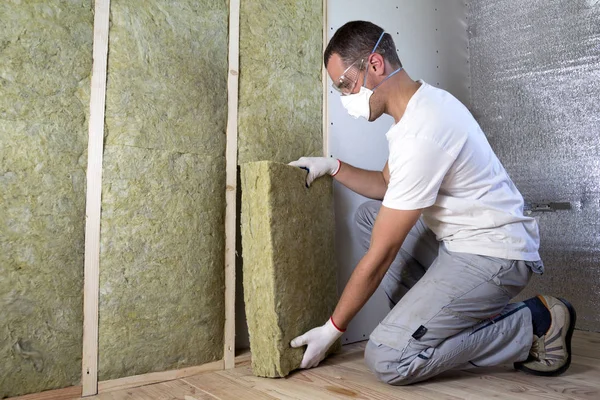 Worker insulating a room wall with mineral rock wool thermal insulation., Stock image