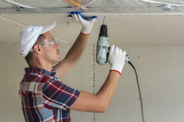 Alçıpan sabitleme Gözlük Genç adam metal çerçeve parlak alüminyum folyo ile yalıtımlı tavanda Elektrikli tornavida kullanarak tavana askıya. Tadilat, inşaat, do It yourself konsepti.