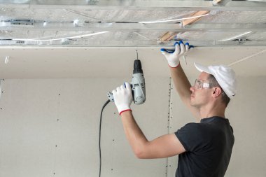 Alçıpan sabitleme Gözlük Genç adam metal çerçeve parlak alüminyum folyo ile yalıtımlı tavanda Elektrikli tornavida kullanarak tavana askıya. Tadilat, inşaat, do It yourself konsepti.