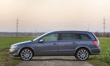 Gri gümüş boş araba çakıl kırsal yol boyunca üzerinde park etmiş yeşil çayırlar, uzak şehir bina ve açık gökyüzü kopya alan arka plan bulanık. Ulaşım, seyahat, Araçlar tasarım konsepti.