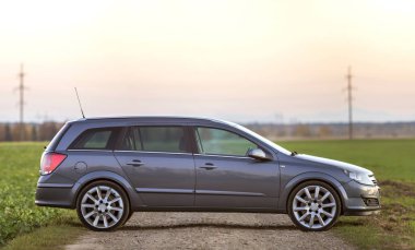 Gri gümüş boş araba çakıl kırsal yol boyunca üzerinde park etmiş yeşil çayırlar, uzak şehir bina ve açık gökyüzü kopya alan arka plan bulanık. Ulaşım, seyahat, Araçlar tasarım konsepti.