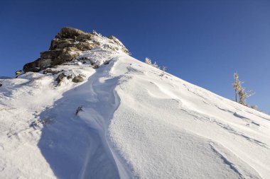 Güzel kış manzarası. Dik dağ yamacı, beyaz derin karla kaplı, uzak odunsu dağ manzarası ufuk çizgisine kadar uzanıyor ve mavi gökyüzü üzerinde parlak güneş ışınları var..
