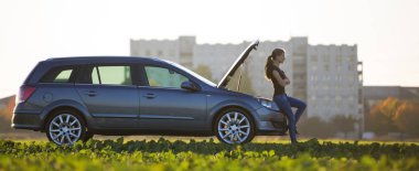 Araba ile genç çekici kadın hood yeşil çayır üzerinde bulanık apartmanın açık ve parlak gökyüzü kopya alan arka plan açık. Ulaşım, araç sorunları ve arıza kavramı.