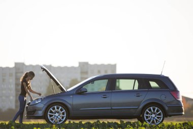 Açık gökyüzü kopya alan arka plan üzerinde yağ çubuğu kullanarak haşhaş kukuleta ile bir araba motorunun kademede petrol kontrol genç çekici kadın. Ulaşım, araç sorunları ve arıza kavramı.