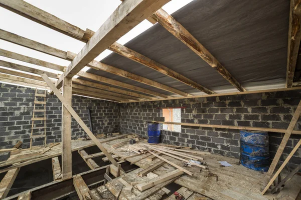 Spacious attic room under construction and renovation. Energy saving walls of large hollow foam insulation blocks and temporary wooden scaffolding, long logs as roof frame. Construction, masonry.