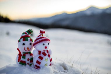 İki küçük komik oyuncaklar kardan adam örme şapka içinde bebek ve arka plan açık havada üzerinde bulanık dağlar derin karda eşarp manzara. Mutlu yeni yıl ve mutlu Noeller tebrik kartı Tema.