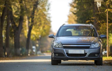 Gri parlak boş araba önden görünümü parlak güneşli gün sokak lâmbası direği bulanık yeşil ve sarı ağaçlar bokeh arka plan üzerinde asfalt yolda sakin bölgede park etmiş. Ulaşım ve Park kavramı.