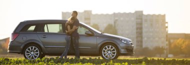 Aşk, uzun at kuyruğu ve yakışıklı adam birlikte gümüş renkli araba bulanık apartman ve berrak gökyüzü kopya alan arka plan yeşil alanını ayakta ince çekici kadın genç çift.