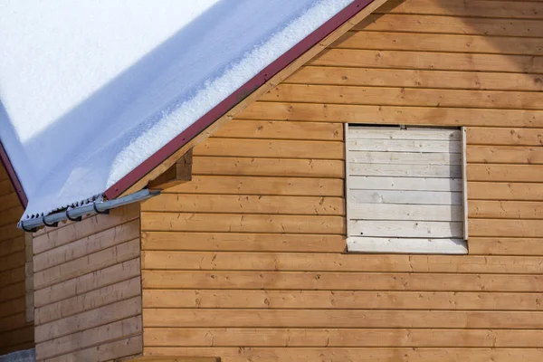 Detail of new wooden ecological traditional cottage of natural lumber materials with steep roof covered with snow on sunny winter day. Old traditions and modern professional construction concept.