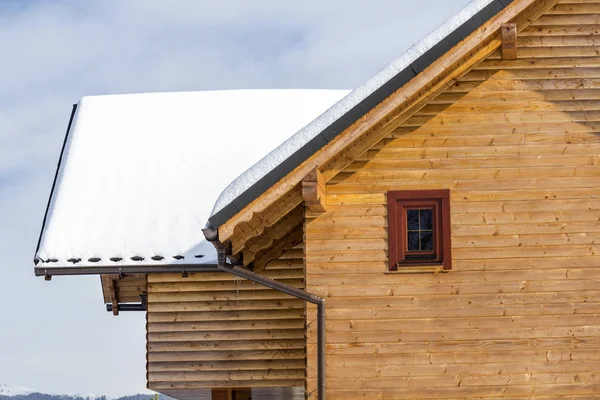 Detail top of wooden ecological traditional cottage of lumber materials with steep roof, attic rooms covered with snow on sunny winter day. Old traditions and modern professional construction concept.