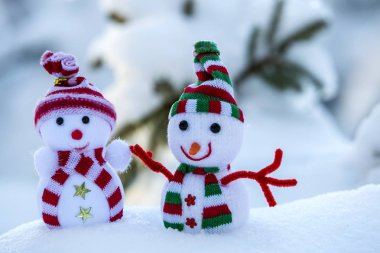 İki komik oyuncak bebek kardan adam örgü şapkalı ve eşarplı açık havada, çam ağacı dalının yanında. Mutlu yıllar ve Mutlu Noeller tebrik kartı.