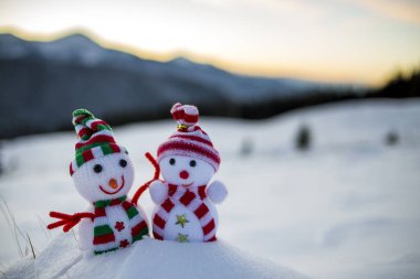 İki küçük komik oyuncaklar kardan adam örme şapka içinde bebek ve arka plan açık havada üzerinde bulanık dağlar derin karda eşarp manzara. Mutlu yeni yıl ve mutlu Noeller tebrik kartı Tema.
