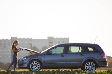 Altında gümüş renkli araba bakıyor duran genç çekici kadın açık gökyüzü kopya alan arka plan üzerinde başlık attı. Ulaşım, araç sorunları ve arıza kavramı.