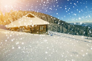 Kış Noel manzarası. Beyaz kardaki insan ayak izleri küçük ahşap çoban kulübesinde, ladin ormanında, odunsu karanlık dağ sıralarında, açık mavi gökyüzünde büyük kar taneleri kopyalama alanı arka planında..