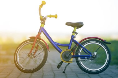 Sol yan stand bulanık parlak bokeh arka plan üzerinde boş döşeli cadde ortasında desteklenen çocuk parlak renkli mavi, sarı ve kırmızı bisiklet Close-up. Çocuk aktif yaşam tarzı kavramı.