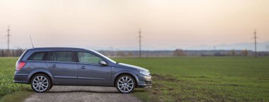 Gri gümüş boş araba çakıl kırsal yol boyunca üzerinde park etmiş yeşil çayırlar, uzak şehir bina ve açık gökyüzü kopya alan arka plan bulanık. Ulaşım, seyahat, Araçlar tasarım konsepti.