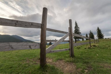 Yeşil çimenli Vadisi yamaç ilkel ahşap çit ve kapı ile panoramik yaz görünümünü gündoğumu, mavi bulutlu gökyüzü altında uzak odunsu sisli dağda. Güzellik, Doğa ve kavram seyahat.