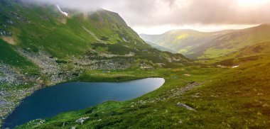 Yeşil vadi ve küçük turistik çadır rocky Mountain mavi göl fantastik geniş huzurlu görünümü ile alçak bulutlar kaplı kar yamalari ile. Güzellik, Doğa, turizm ve seyahat kavramı.