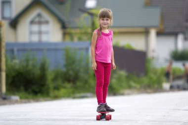 Casual giyim stand üzerinde kaykay üzerinde gülümseyen kız Genç ve güzel uzun saçlı sarışın çocuk yaz güneş parlak banliyösü street tarafından üzerinde arka plan bulanık yaktı. Çocuk Aktiviteleri, Oyunlar ve eğlence kavramı.