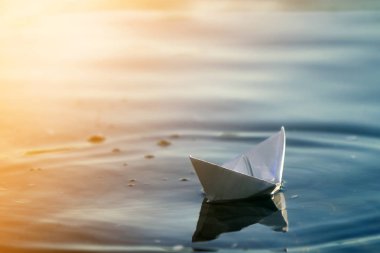 Basit küçük beyaz origami kağıt tekne sessizce parlak yaz göğün altında açık mavi nehir veya deniz suyu yüzen Close-up. Özgürlük, düşler ve fantasies kavramı, boşaltmak arka plan.