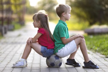 İki sevimli sarışın çocuk profil portresi, futbol topu boş güneşli banliyösü üzerinde oturan uzun saçlı kız ve erkek gülümseyen bulanık yol yaz parlak arka plan döşeli. Çocuk oyun ve eğlence kavramı.