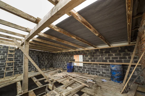 Two-storied building under construction and renovation. Perspective view of energy saving walls of large hollow foam insulation blocks and bricks, temporary wooden scaffolding, beams as roof frame.