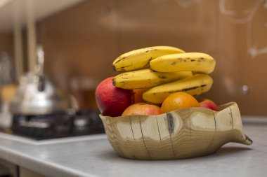 Ahşap tabak kase taze lezzetli lezzetli meyve elma ile. muz ve portakal beyaz mutfak masasında ışık arka plan bulanık.