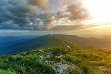 Geniş Yataklı güneş doğarken yaz. Parlayan turuncu güneş mavi bulutlu gökyüzü yeşil çimenli tepe yumuşak çim ve uzak dağ üzerinde yükselterek sabah sis ile kaplı. Doğa kavramının güzellik.