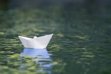 Basit küçük beyaz origami kağıt tekne sessizce parlak yaz göğün altında açık mavi nehir veya deniz suyu yüzen Close-up. Özgürlük, düşler ve fantasies kavramı, boşaltmak arka plan.