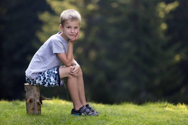 Sersem ağaç kütüğü taze yeşil çimenli takas parlak yaz gününde üzerinde oturan çocuk çocuk gülümseyen Genç Sevimli sarışın yeşil kopya alan arka plan bulanık. Rekreasyon, açık havada faaliyetleri kavramı.