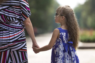 Arkadan görünüşü moda mavi elbise ve genç kadının elini açık havada bulanık renkli güneşli yaz bokeh arka planda tutarak güneş gözlüğü güzel uzun sarı saçlı kız çok genç çocuk.