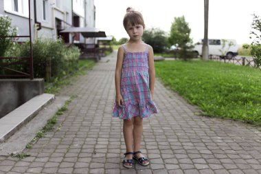 Apartmanın ne yazık ki kamera seyir önce güneşli kaldırım üzerinde tek başına duran rahat yazlık elbise kız Genç ve güzel küçük sarışın mutsuz huysuz arkadaşı olmayan çocuk. Çocuk sorunları kavramı.