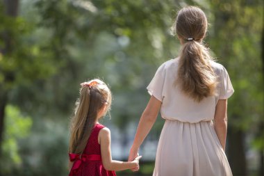 Küçük sarışın uzun saçlı çocuk kız moda elbiseler birlikte bulanık renkli güneşli bokeh arka plan açık havada sıcak güneşli gün tutuşup yürürken ince ince annesi ile arkadan görünüm.