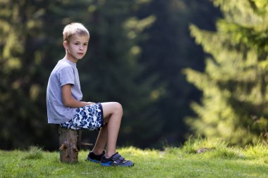Sersem ağaç kütüğü taze yeşil çimenli takas parlak yaz gününde üzerinde oturan çocuk çocuk gülümseyen Genç Sevimli sarışın yeşil kopya alan arka plan bulanık. Rekreasyon, açık havada faaliyetleri kavramı.