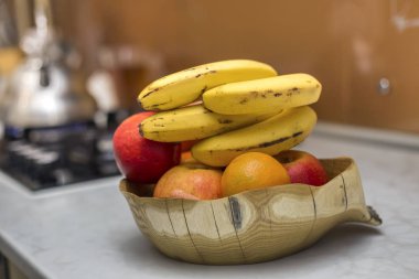 Ahşap tabak kase taze lezzetli lezzetli meyve elma ile. muz ve portakal beyaz mutfak masasında ışık arka plan bulanık.