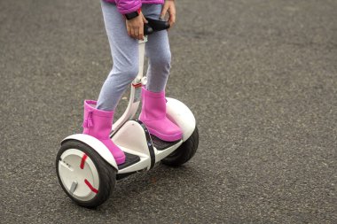 Çocuk kız bacaklar parlak pembe kauçuk Close-up binme segway güneşli asfalt sokak kopya alan arka plan üzerinde botlar. Modern teknoloji, yol ve aktif yaşam tarzı çocuk emniyeti.