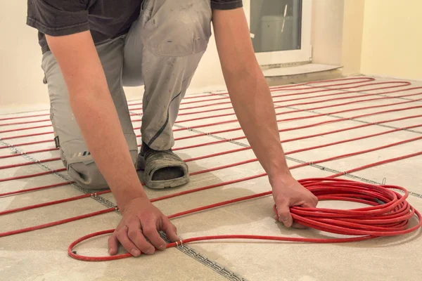 Electrician installing heating red electrical cable wire on cement floor in unfinished room. Renovation and construction, comfortable warm home concept.