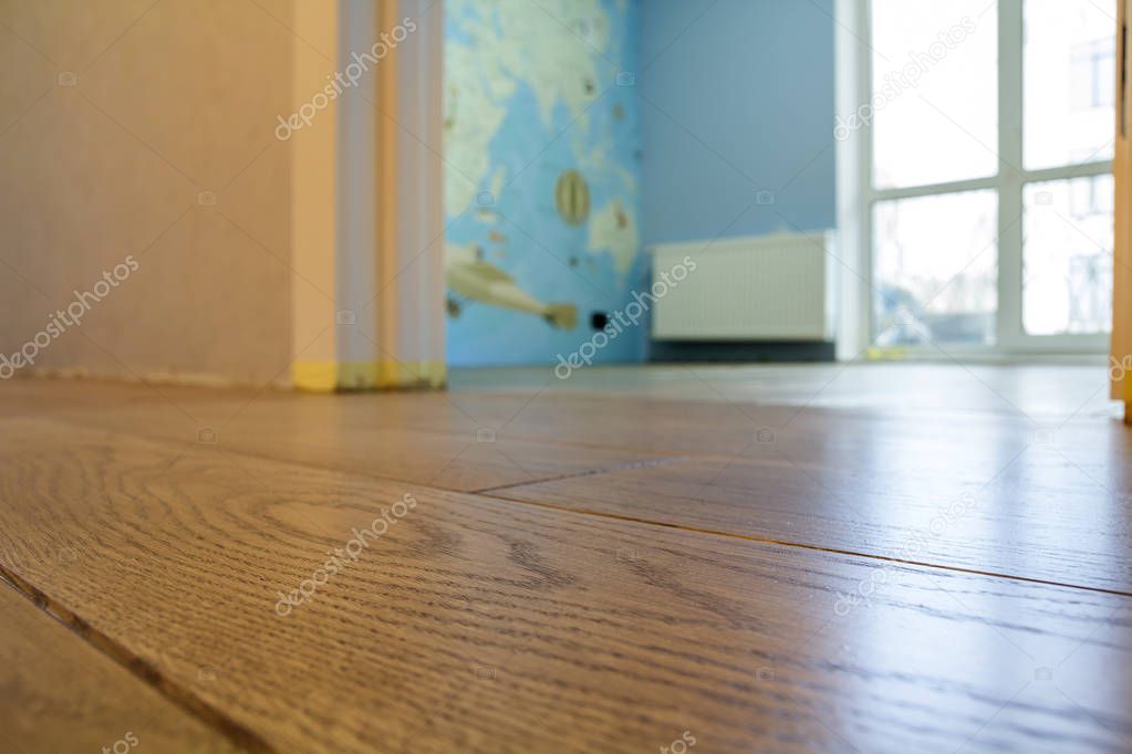 Spacious empty room, wooden floor light brown polished surface background in new apartment interior, beige walls, blurred glass window or door opening.