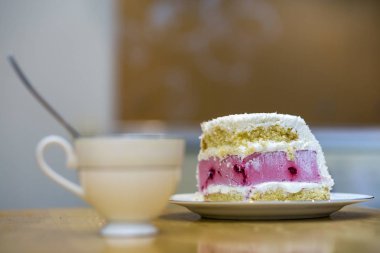 Parçasıyla taze lezzetli lezzetli ev yapımı meyve bisküvi beyaz ve pembe kremalı kek mutfak masasında porselen Kupası hafif bulanık kopya alan arka plan üzerinde beyaz tabak.