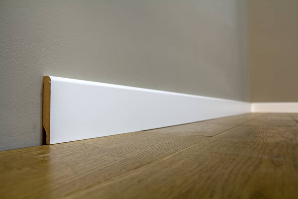 Деревянный или пластиковый белый пол плинтус установки в большой пустой комнате на деревянном полу и белой штукатуркой штукатурки стен фона. Детали интерьера
.