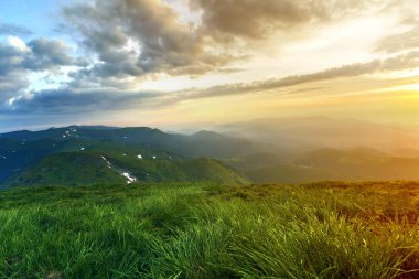 Geniş Yataklı güneş doğarken yaz. Parlayan turuncu güneş mavi bulutlu gökyüzü yeşil çimenli tepe yumuşak çim ve uzak dağ üzerinde yükselterek sabah sis ile kaplı. Doğa kavramının güzellik.